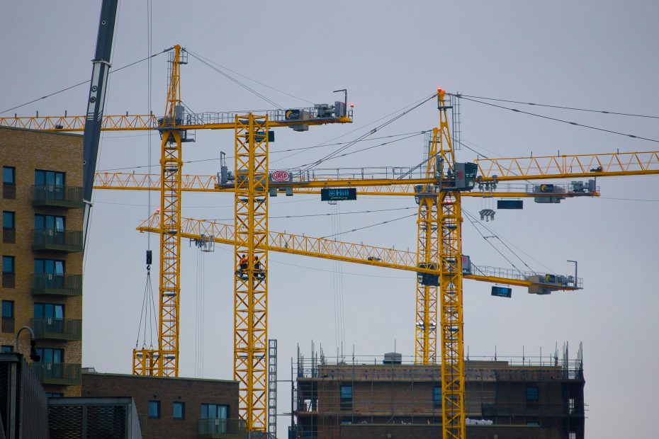 lots of yellow builders cranes against a grey sky